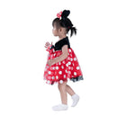 Toddler wearing a red and black Minnie Mouse costume with polka dots, complete with ears and a bow, walking.