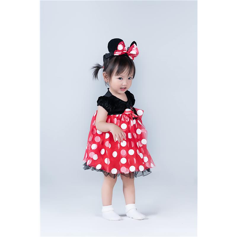 Toddler wearing a red Minnie Mouse costume with polka dots, black ears, and a matching bow, smiling.