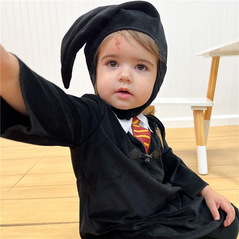 Toddler dressed in a black Harry Potter costume, featuring a hooded cape and a red-and-yellow tied scarf.