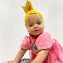 Infant wearing a pink Princess Peach costume with puff sleeves and a yellow crown headband, crawling on a textured surface.