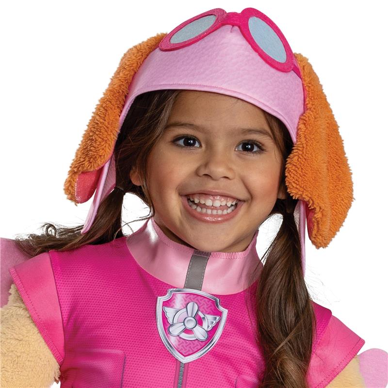 Toddler girl wearing a pink Paw Patrol Skye costume with goggles and dog-ear headband, smiling joyfully.