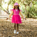 Toddler girl wearing a pink Paw Patrol Skye costume with a tutu, dog-ear hat, and smiling in a park setting.
