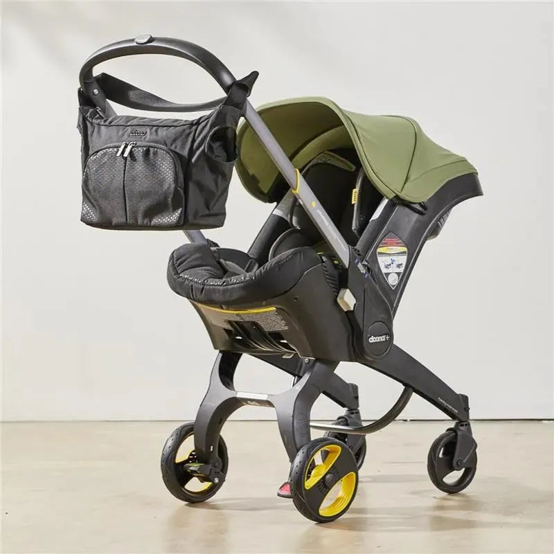 Essentials bag in Nitro Black attached to a Doona stroller with a green canopy and padded seat.