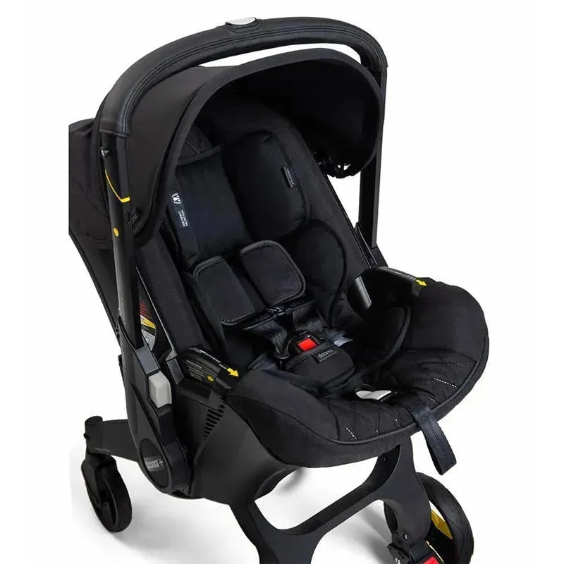 Doona Infant Car Seat with Base & Stroller in Midnight featuring a sleek black design, safety harness, and wheels for mobility.