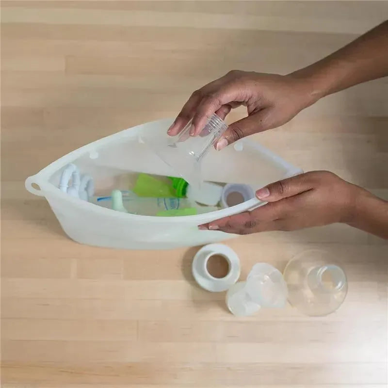 Hands placing a baby bottle in a Dr Brown silicone microwave steam sterilizer bag on a wooden surface.