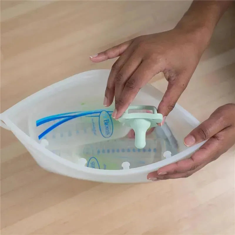 Hands holding a Dr Brown 100% silicone microwave steam sterilizer bag with a green sealing clip and measurement markings inside.