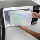 Reusable silicone microwave steam sterilizer bag being held near a microwave, containing various baby items inside.
