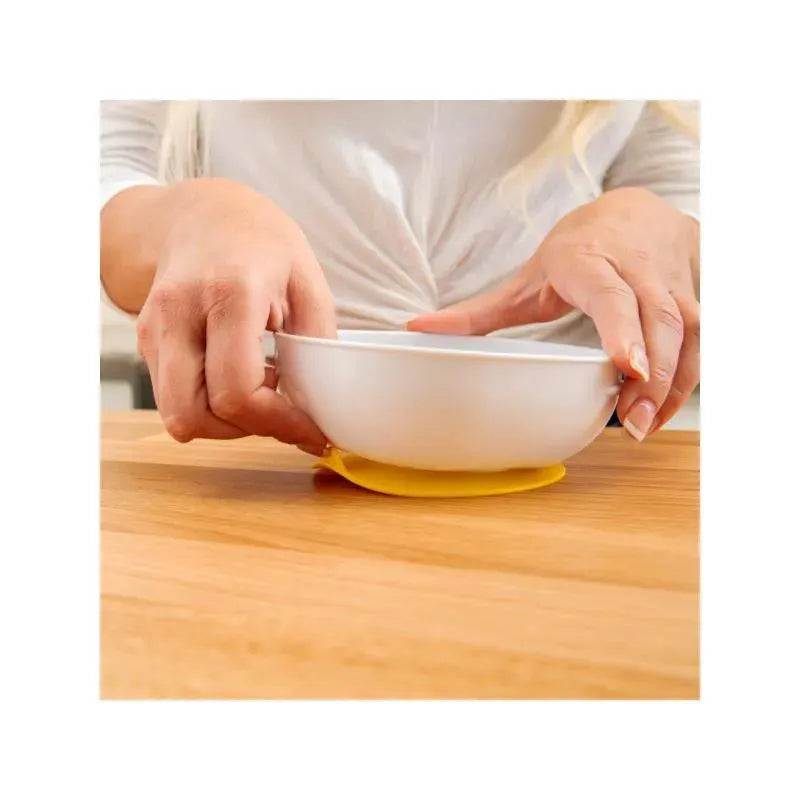 Suction bowls secured on a wooden surface, with a person placing a bowl on a yellow no-slip mat.