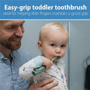 Toddler using a green dinosaur toothbrush with easy-grip handle, helped by an adult in a bathroom setting.