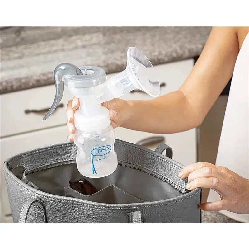 Manual breast pump with soft silicone shield by Dr. Brown, held above a gray bag with visible compartments.