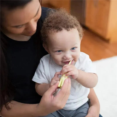 Young child with curly hair brushing teeth with a yellow training toothbrush, held by an adult.
