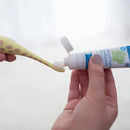 Training toothbrush with giraffe design held over a tube of fluoride-free strawberry toothpaste, with paste applied on bristles.