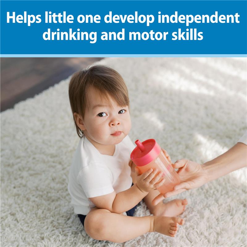 Toddler sitting on a rug, holding a pink straw training cup, with an adult’s hand offering the cup.