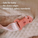 Pink pacifier clip with a striped fabric strap, featuring text highlighting safety features for babies.