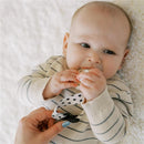 Baby holding a pacifier, with a polka-dotted clip being attached to their clothing.