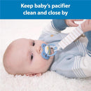 Baby relaxes on a soft surface, holding a pacifier attached to a striped clip, promoting cleanliness and accessibility.