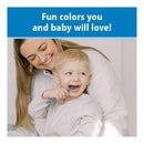 Toddler smiles while brushing teeth with a blue toothbrush, seated on a lap of a smiling caregiver in cozy attire.