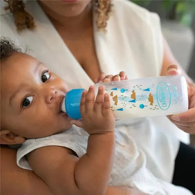 Narrow anti-colic baby bottle with a blue cap, held by an infant, featuring nature-themed designs.