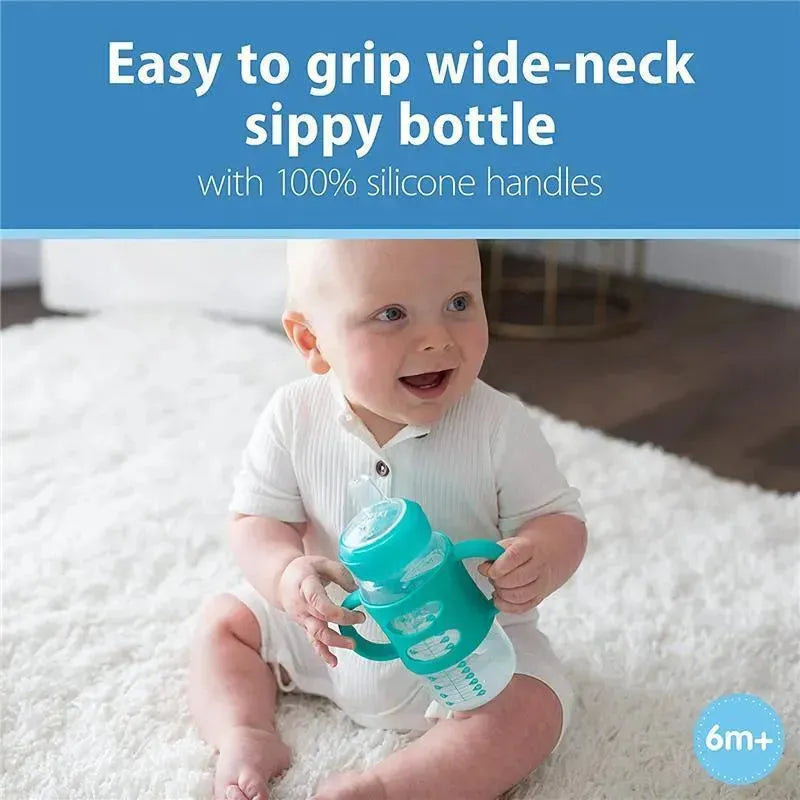 Light blue wide-neck sippy bottle with silicone handles held by a smiling baby sitting on a soft rug.