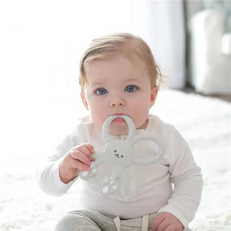 Gray Flexees Bunny Silicone Teether held by a baby sitting on a soft surface, featuring a rabbit design with textured handles.