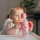 8oz Narrow Sippy Straw Bottle with silicone handles in pink, held by a baby sitting at a table.