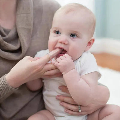 Silicone finger toothbrush held by an adult assisting a baby, who appears engaged and curious.