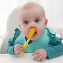 A baby with blue eyes holds a yellow spoon, with food smeared on their face and a teal bib on.