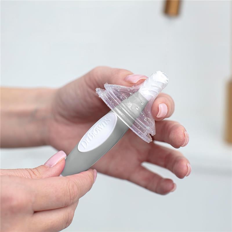 Cleaning brush with a silicone tip and ergonomic handle designed for baby bottles, being held with water droplets visible.