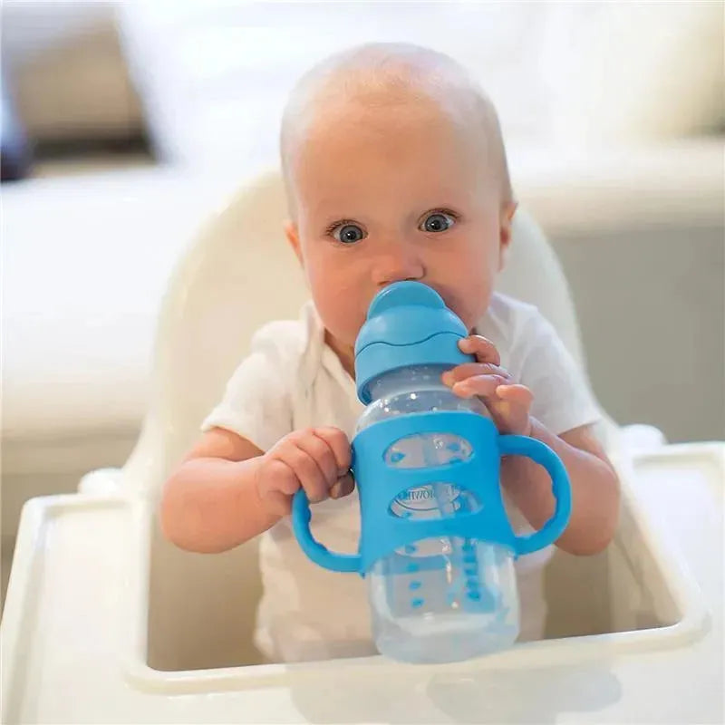 Wide-neck blue sippy straw bottle with silicone handles held by a baby, who is seated in a high chair.