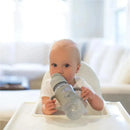 Wide-neck sippy straw bottle with silicone handles in gray, held by a baby sitting in a high chair.