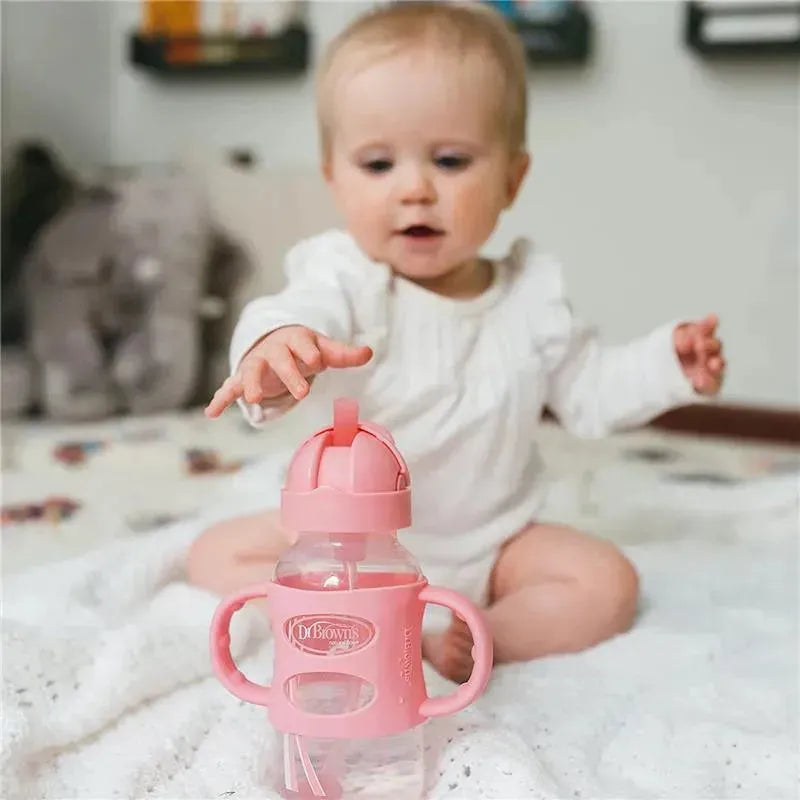 Wide-neck pink sippy straw bottle with silicone handles, featuring a baby reaching for it.