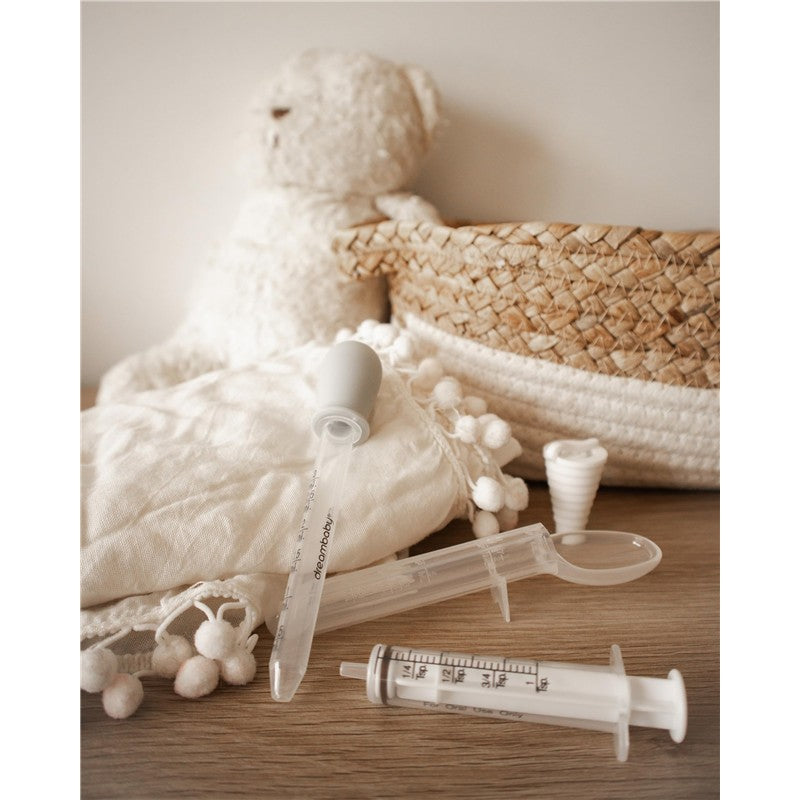 Dreambaby Medicine Set featuring a medicine dropper, syringe, and dosing spoon on a soft cloth, with a teddy bear and woven basket in the background.
