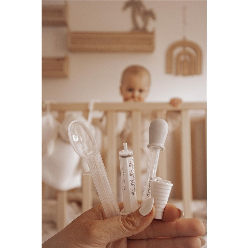 Dreambaby Medicine Set includes a nasal aspirator, a syringe, and a dropper, held by a hand, with a baby in a crib in the background.