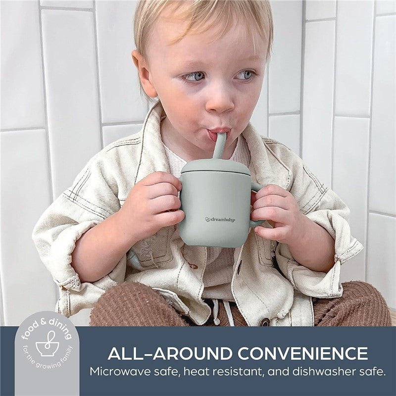 Child holding a seafoam Dreambaby Drink & Snack Cup with a straw, sitting against a tiled background.