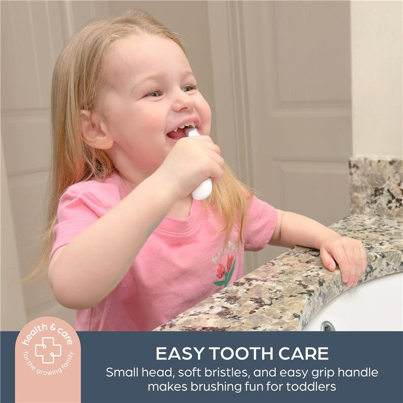 A young girl brushes her teeth with a toddler-friendly toothbrush, smiling at a bathroom sink.