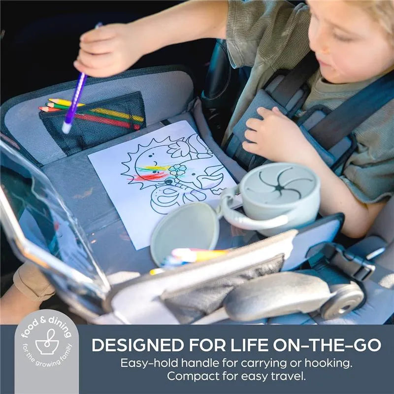 Foldable seafoam snack cup on a car seat tray with a child coloring and colored pencils nearby.
