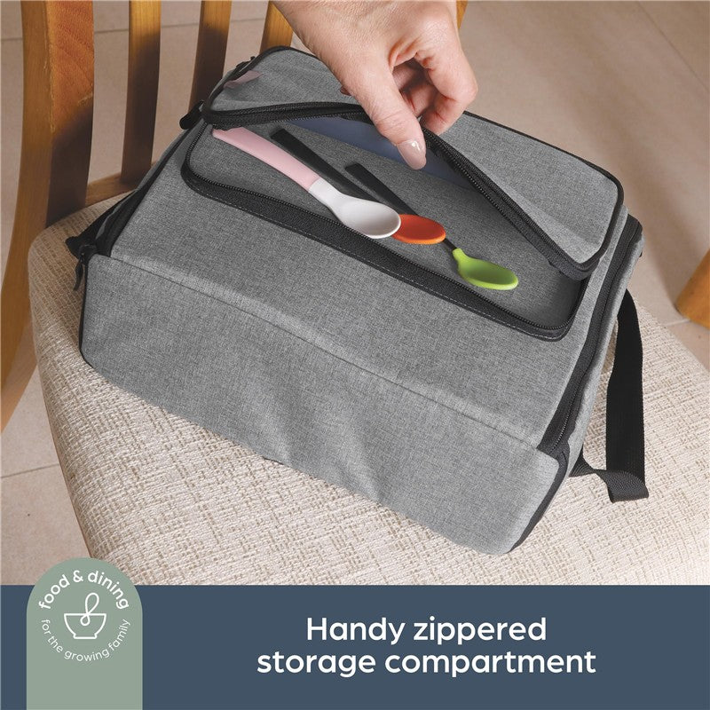 Grey booster seat bag with a zippered compartment containing colorful spoons, placed on a chair.