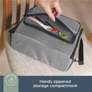 Grey booster seat bag with a zippered compartment containing colorful spoons, placed on a chair.