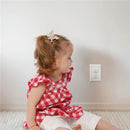 Toddler in a red checkered shirt sits near a wall outlet, promoting safety with outlet plugs.