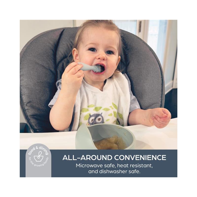 A toddler sitting in a high chair uses a silicone spoon to eat from a light green bowl containing food, showcasing the Dreambaby Scoop and Mash product.