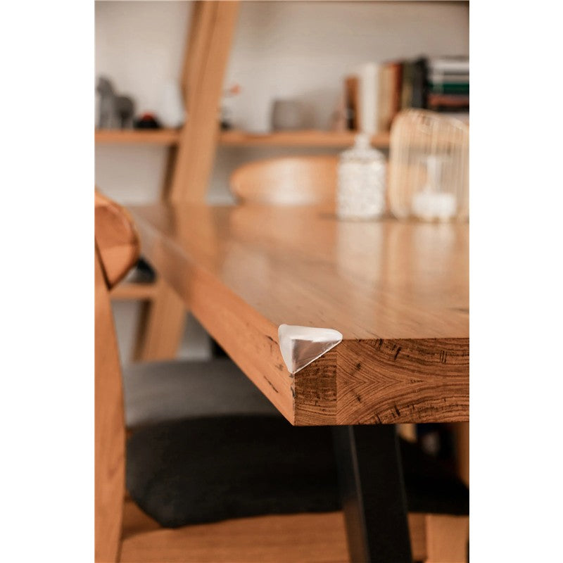 Soft Touch Corner Cushion positioned on the sharp edge of a wooden table to provide safety and reduce injury risk.