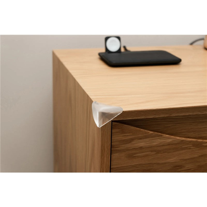 Transparent corner cushion placed on a wooden furniture edge, designed for safety to prevent injuries.