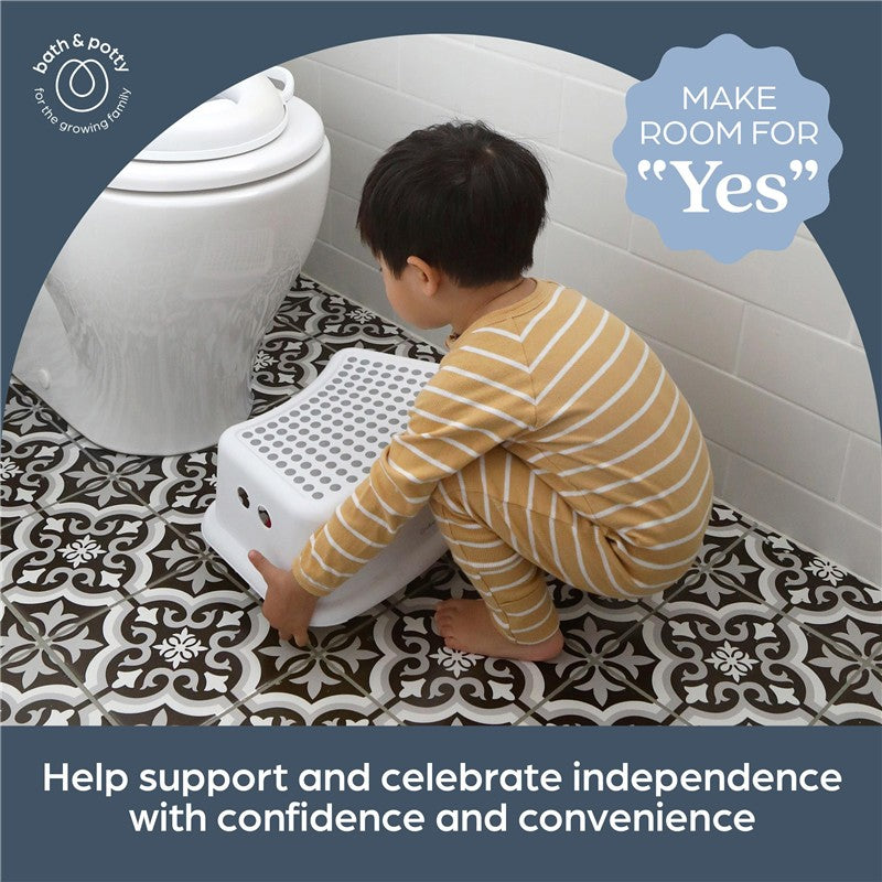 Child dressed in striped pajamas using a Dreambaby Step Stool with grey dots to reach a toilet, emphasizing independence.