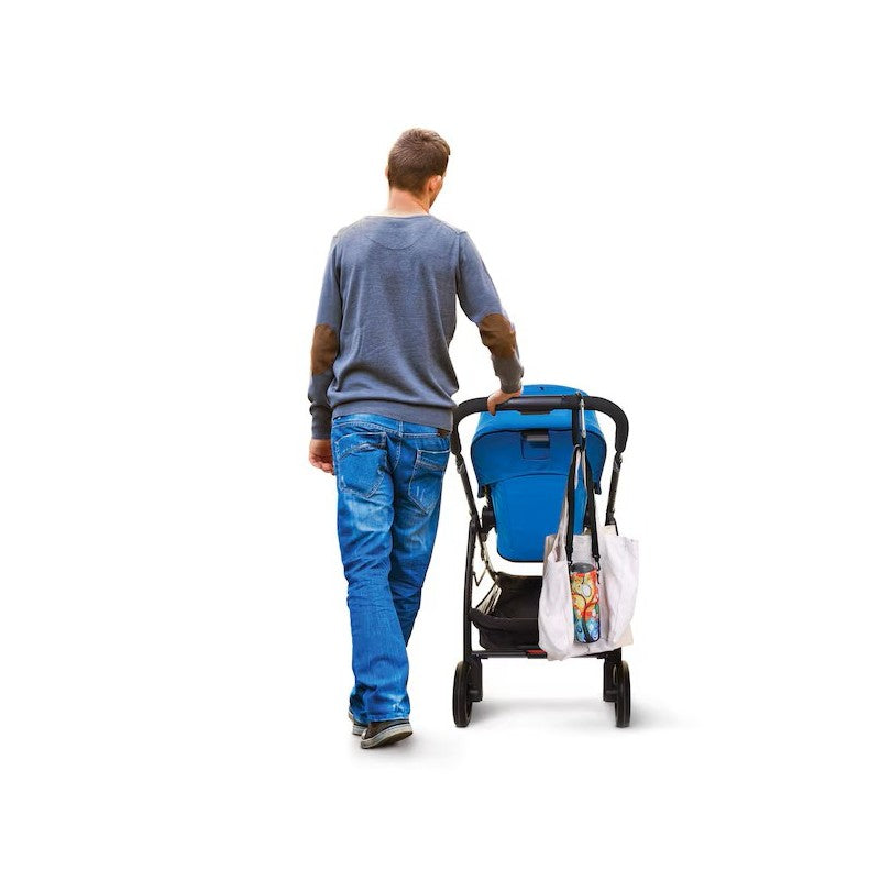 A person walking away from the camera, pushing a stroller with a blue seat, and carrying a tote bag attached.