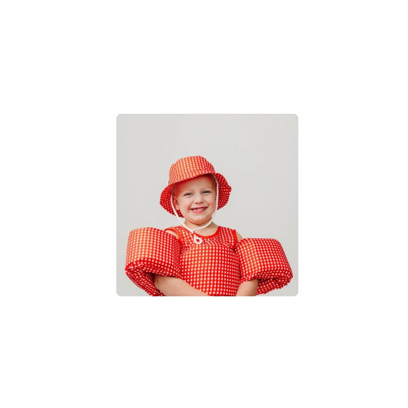 Smiling child wearing a red gingham float suit and matching hat, designed for water safety.