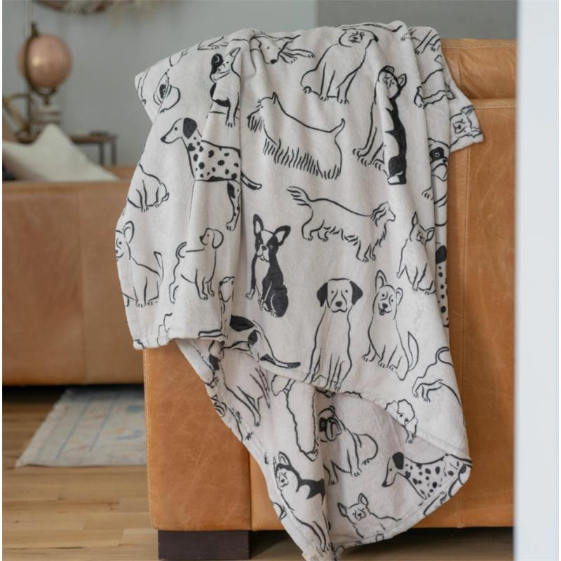 Double-sided throw blanket featuring various dog illustrations, draped over a brown leather couch.