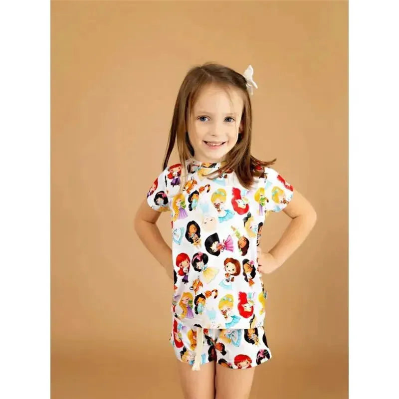 Young girl smiling while wearing a colorful bamboo lounge set featuring princess designs on the top and shorts.