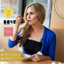 Model wearing the Simple Wishes hands-free breast pump bra, enjoying a snack while using the pump, with award badges displayed.