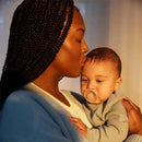 A mother kisses her baby, who is holding a rose-colored pacifier, while being cradled lovingly in her arms.