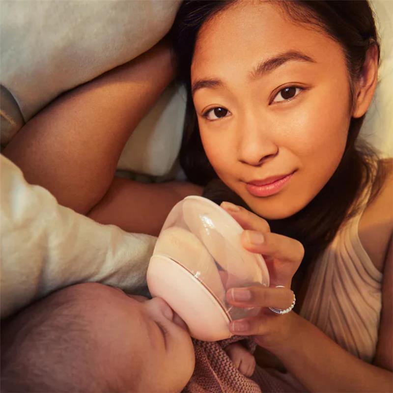 A woman gently feeds a baby with a light-colored glass bottle, showcasing an intimate moment of nurturing.